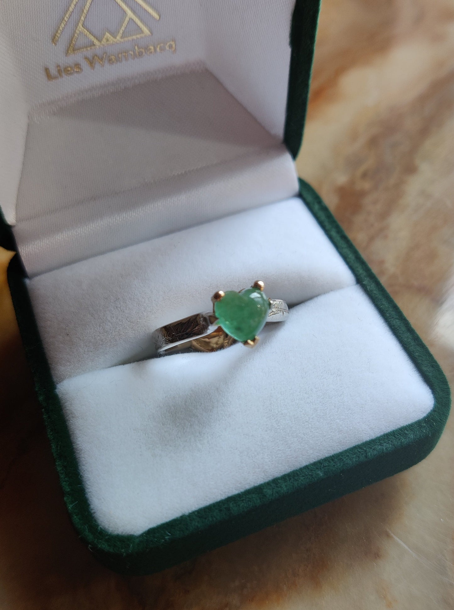 ring in het geel en wit goud. Aan de bovenkant zit er een groen edelsteen hart met pootjes en aan de onderkant van de ring is er een geelgouden oriëntaals geïnspireerd hart. Het groene hart van smaragd is bol.