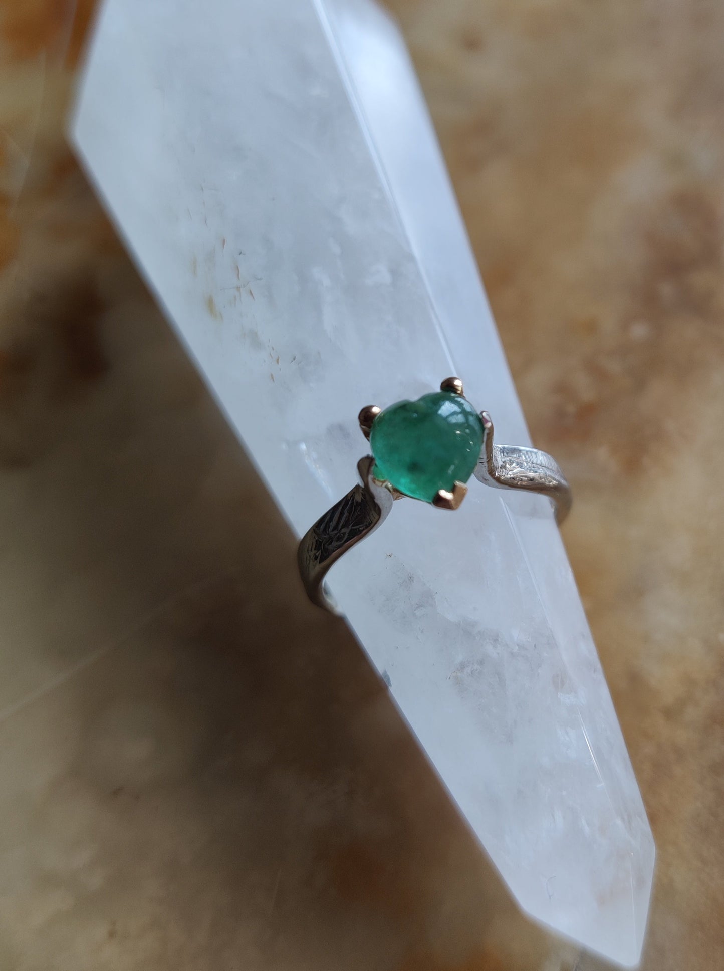 ring in het geel en wit goud. Aan de bovenkant zit er een groen edelsteen hart met pootjes en aan de onderkant van de ring is er een geelgouden oriëntaals geïnspireerd hart. Het groene hart van smaragd is bol.