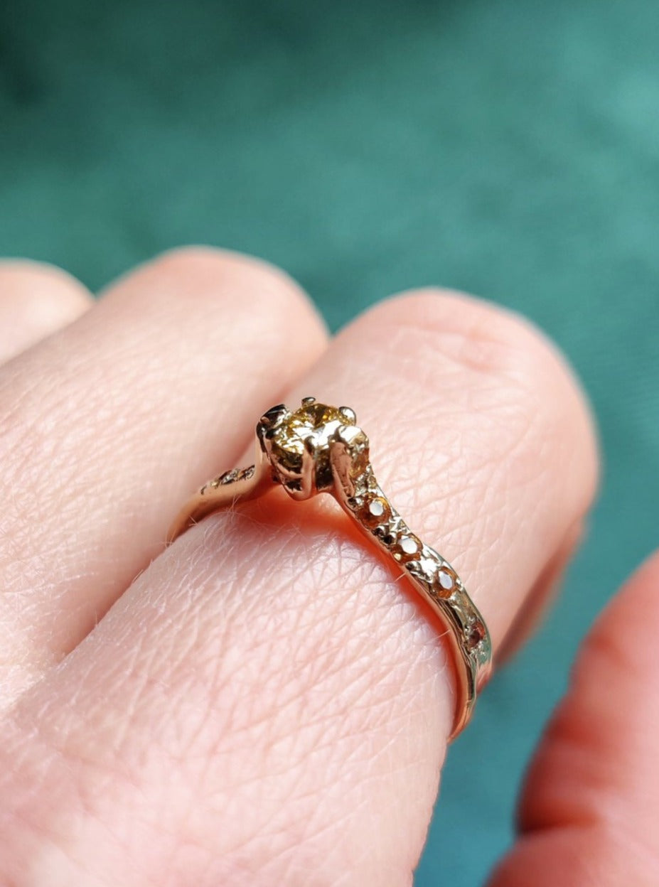 Een verlovingsring waar er maar één van is. Het bandje is wat ruwer, bruter gemaakt. De ring heeft een organisch gevoel en is de combinatie van natuurlijk witgoud en een natuurlijke gekleurde ovalen diamant. Aan de zijkanten zitten oranje saffieren.