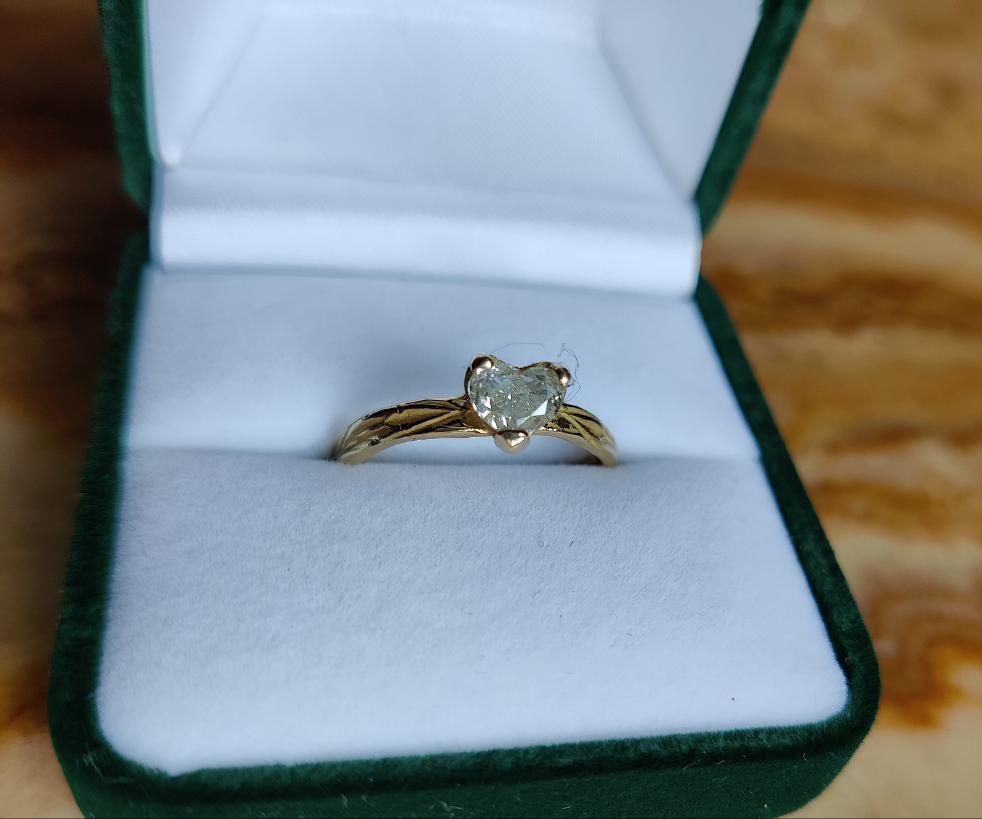Een verlovingsring met hartvormige diamant gezet in pootjes in een organisch bandje. In het bandje zit precies een bloemenpatroon gegraveerd. Het is een organische band met solitair steen.