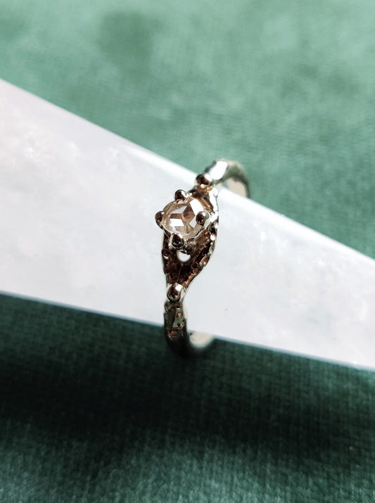 Een verlovingsring met een vintage look and feel in het wit goud. Een solitair met een roosgeslepen diamant dat in een opengewerkt bandje staat.