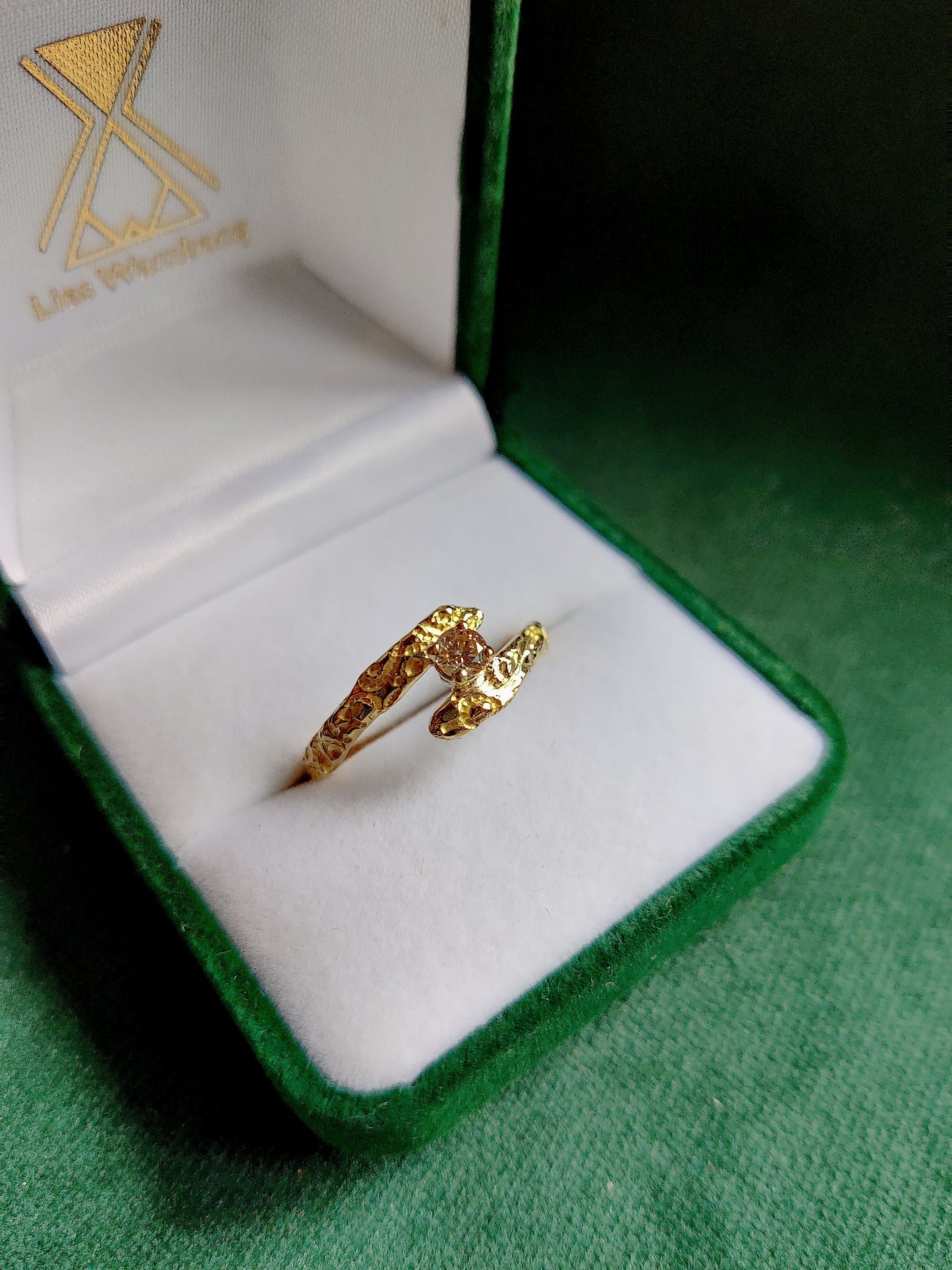 De diamant is gezet in pootjes en staat tussen de open band van de ring. De ring heeft een oriëntaals motief. 