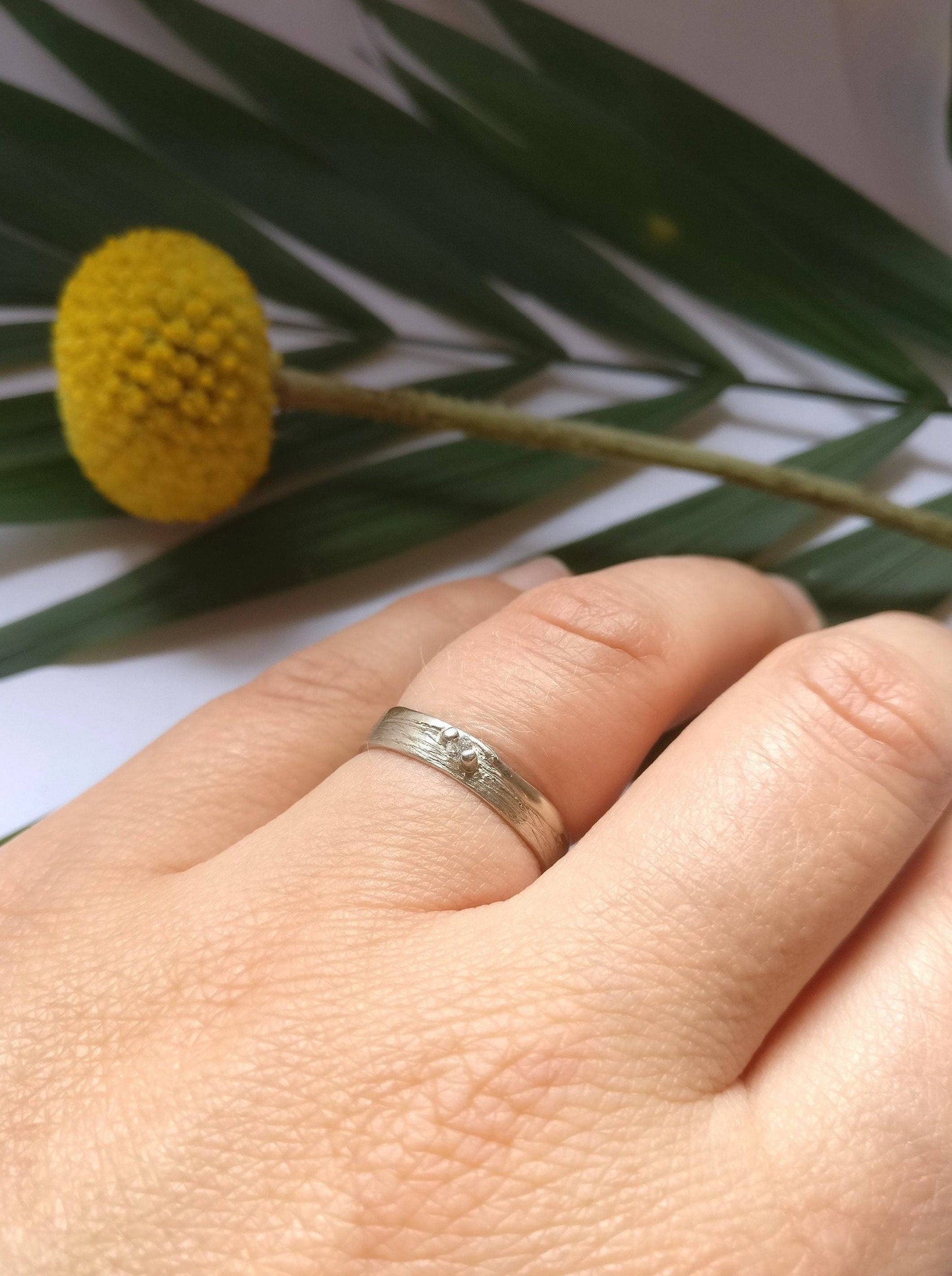 Ring in 18K champagne wit goud met diamant gezet tussen twee bolletjes. Het is een matte ring met geborstelde textuur en een diamantje.